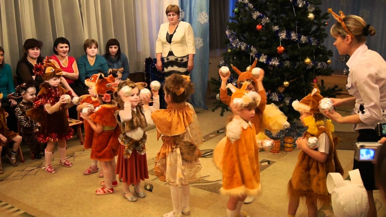 Девочки в костюмах белочек танцуют на новогоднем утреннике в детском саду.