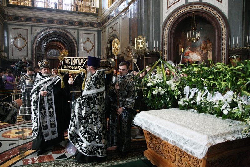 Священнослужители в черных одеждах выносят плащаницу