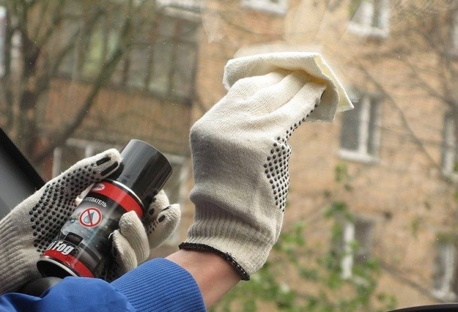 Хозяин автомобиля обрабатывает стекла в салоне специальным аэрозолем против запотевания