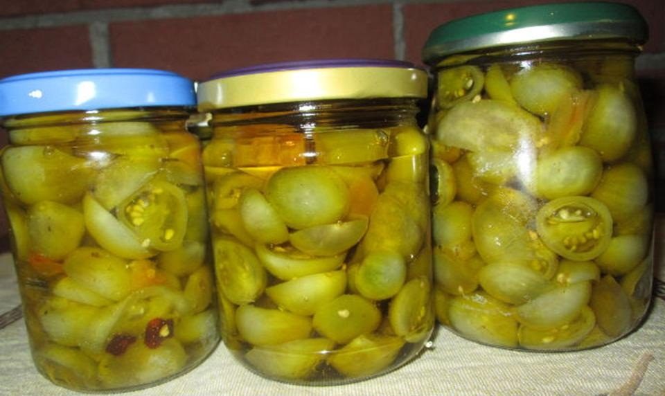 Три банки на столе с маринованными зелеными огурцами, приготовленными по рецепту с кетчупом чили