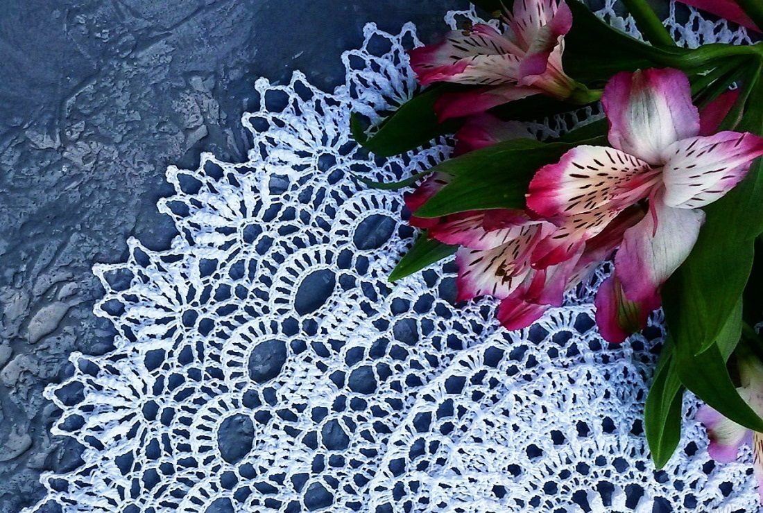 Красивая ажурная салфетка, связанная крючком, лежит на столе с цветами