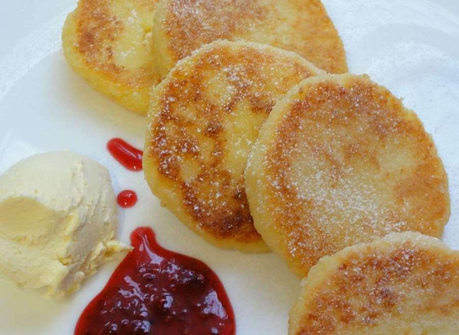 На тарелке несколько ароматных сырников со сметаной и джемом
