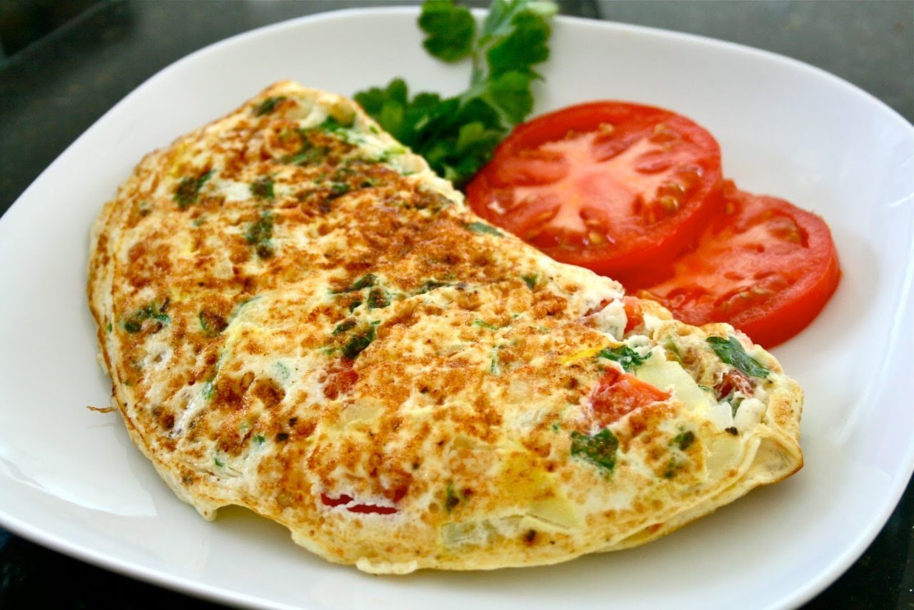 Аппетитный омлет с овощами и колбасками на тарелке с помидорами
