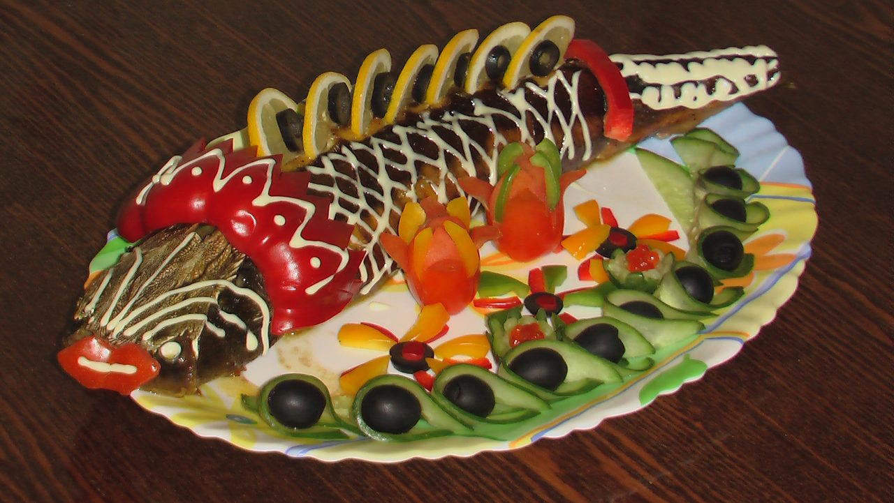 Осетр запеченный в духовке, украшенный оливками, майонезом, овощами