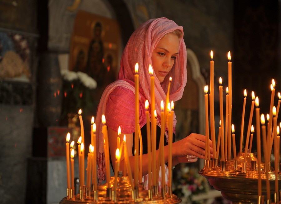 A lány imádkozik a templomban és gyertyákat tesz