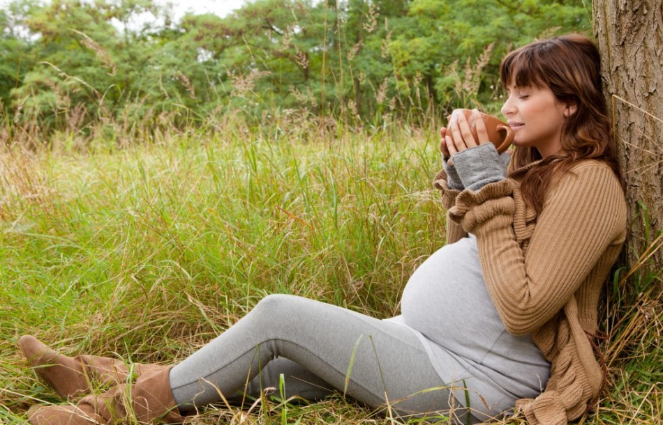 Беременная девушка с удовольствием пьет зеленый чай на природе