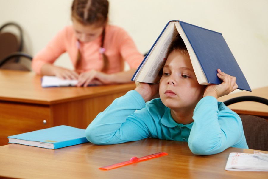Anak sekolah yang lelah di belakang meja ditutupi oleh buku teks terbuka dengan aturan untuk kemunduran nama tengah keluarga wanita