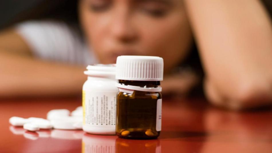 Seorang gadis yang sedih duduk di meja di depan bank terbuka dengan antidepresan saat menurunkan berat badan