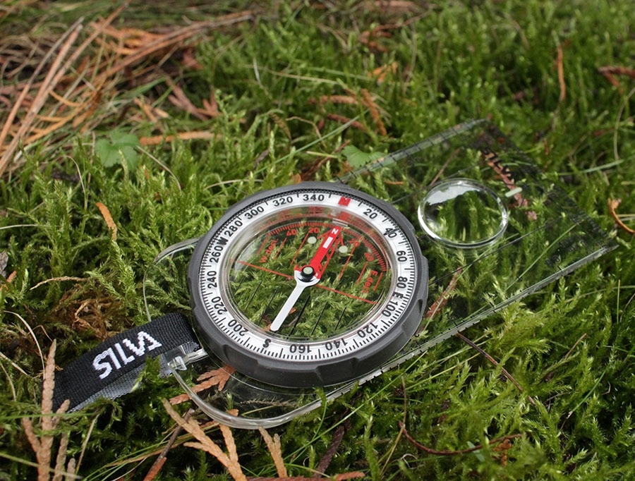 Kompas leži na travi, preden določi kardinalne točke in orientacijo na tleh