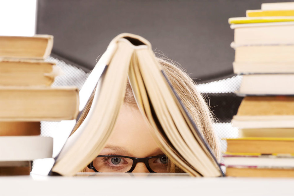 Seorang gadis dalam kacamata mengintip karena buku -buku di mana dia mencari aturan untuk penolakan nama wanita