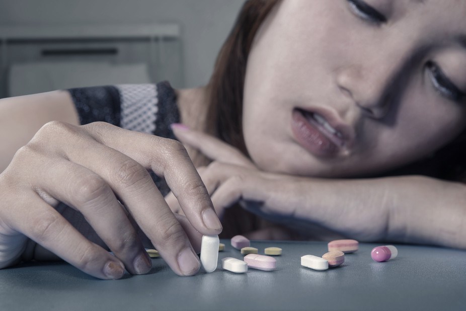Egy tizenéves lány ül egy asztalnál, maroknyi antidepresszánssal