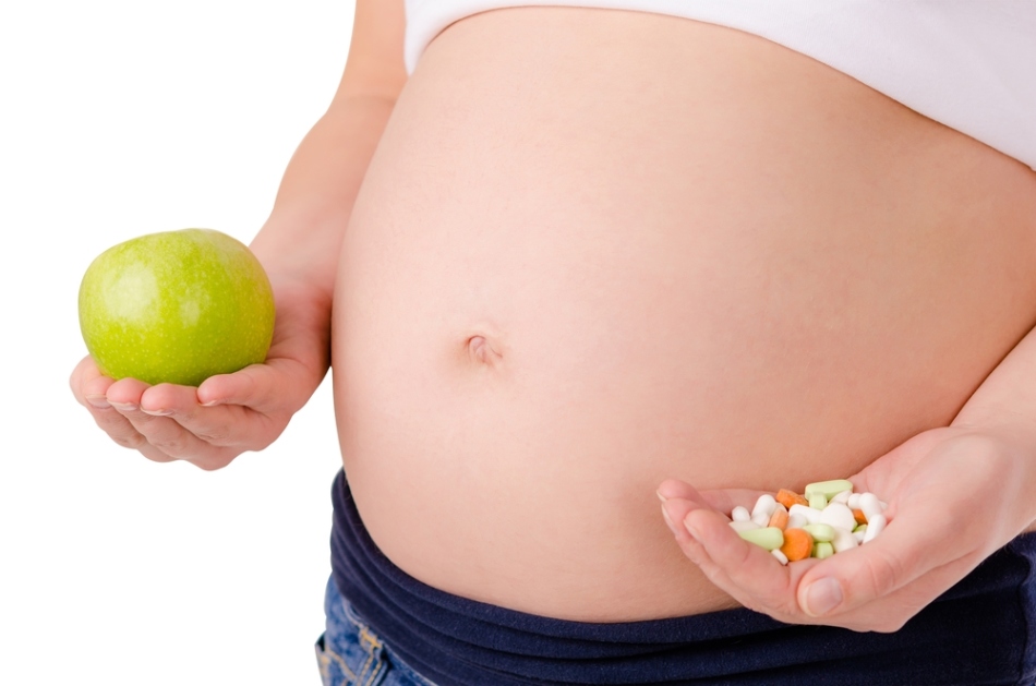 A girl with a large belly holds an apple and a handful of vitamins in her hands