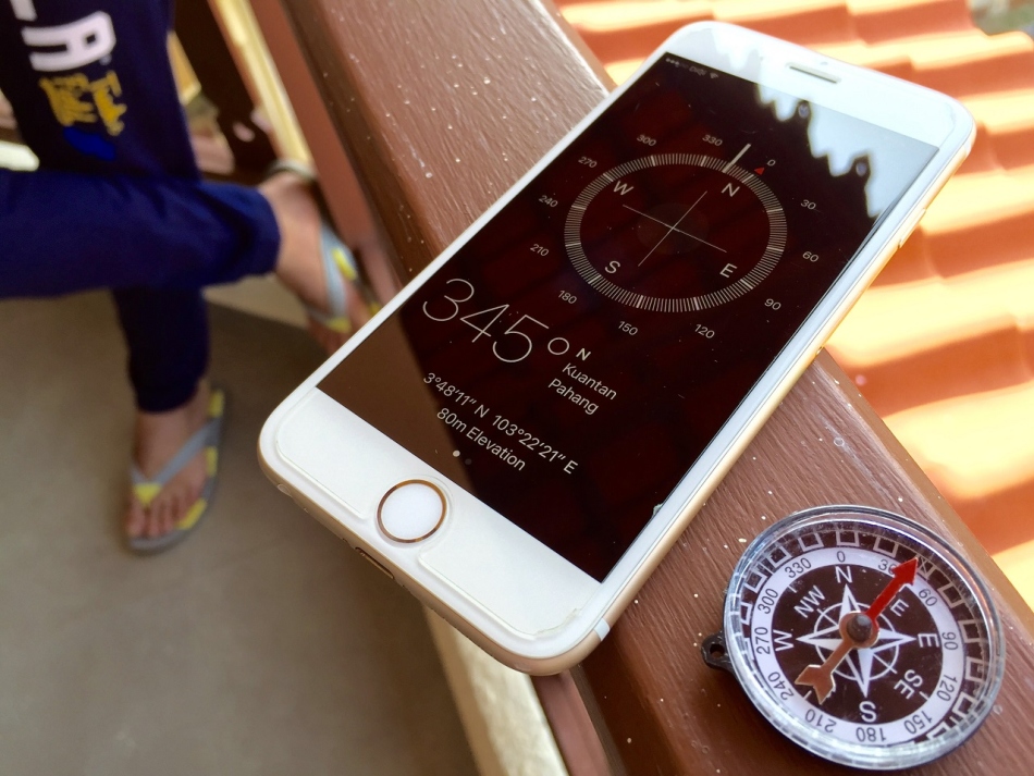 L'iPhone se trouve sur la balustrade avec un programme de boussole ouvert près d'une boussole régulière