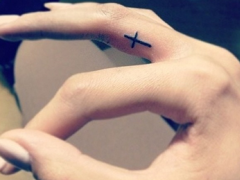 Small tattoo on the finger in the form of a cross