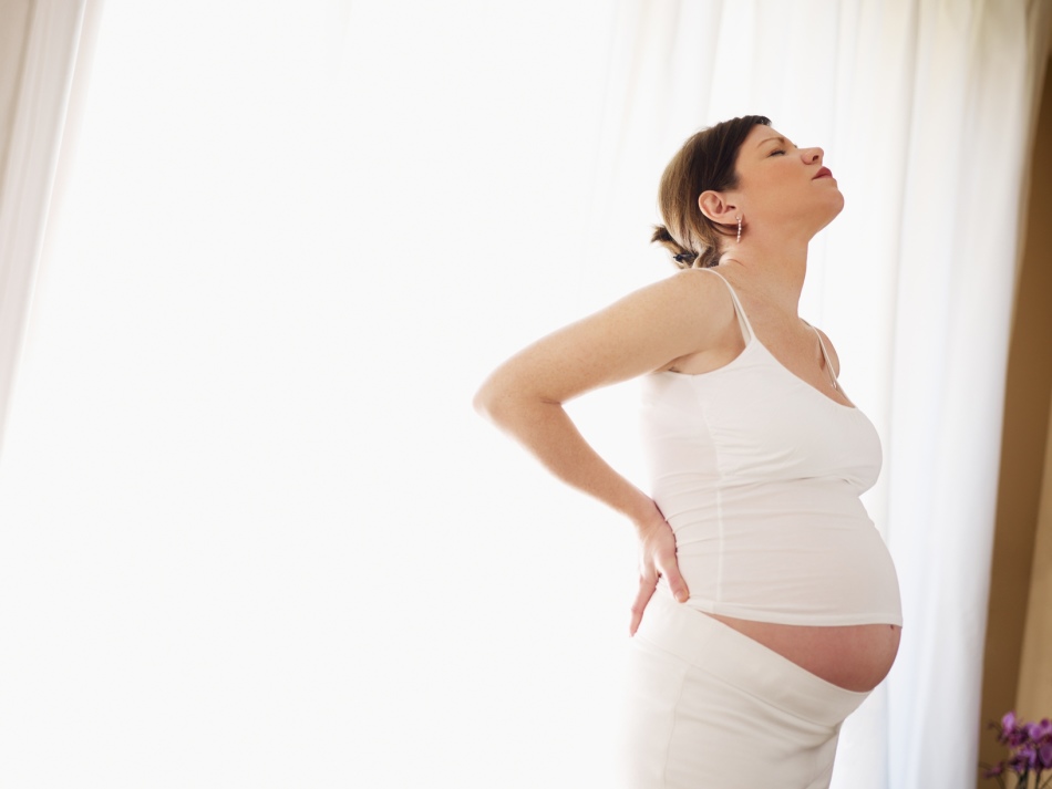 Pregnant woman holds on her lower back