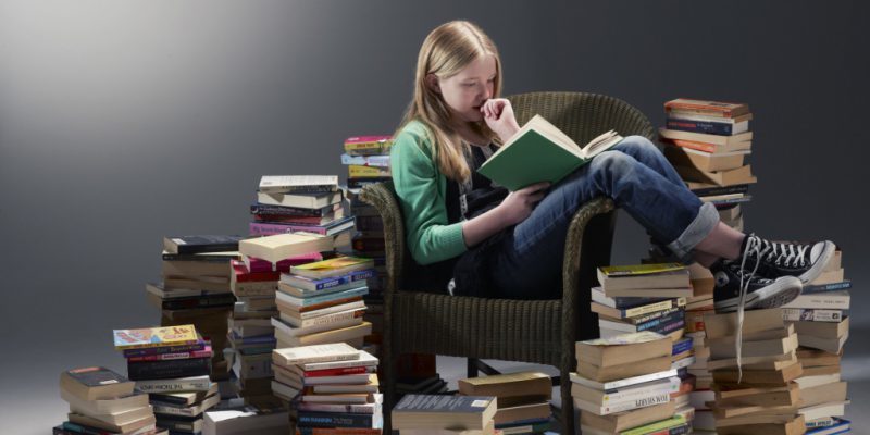 A középiskolás diák egy székben ül, és a könyvek szerint tanulmányozza a ritka szavak jelentését