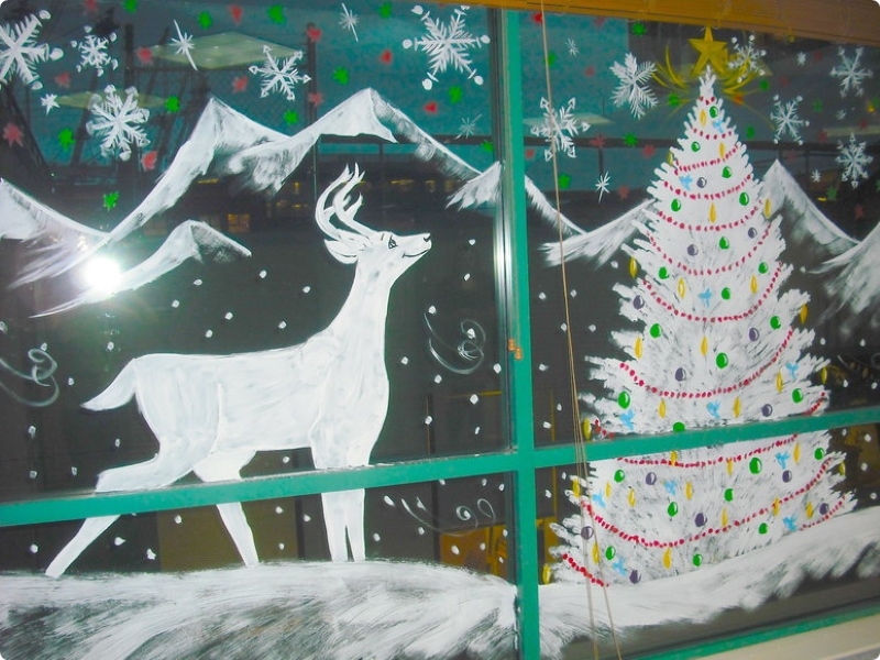 Ein Weihnachtsbaum, Hirsche und Berge werden an der Glaswand gezeichnet