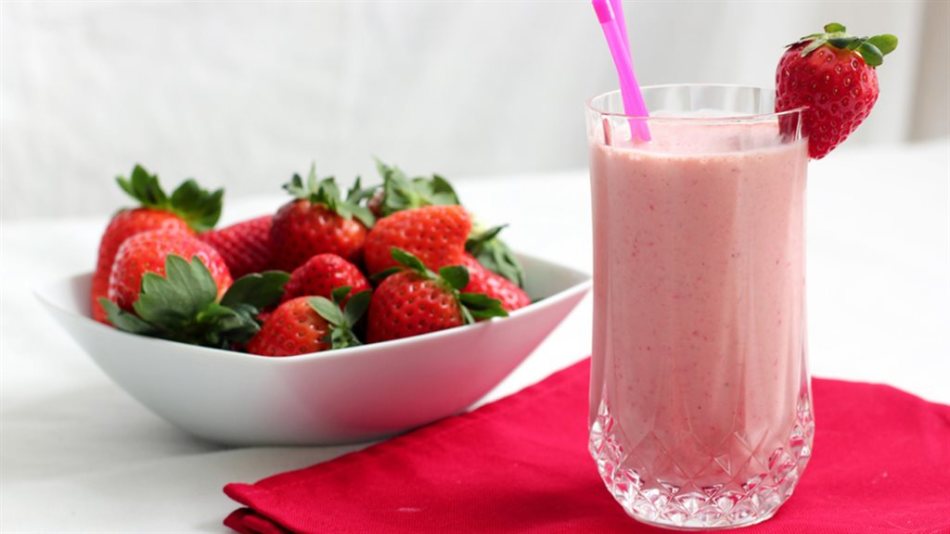 A handful of fresh strawberries in the bowl on the table and strawberry smoothies in a glass