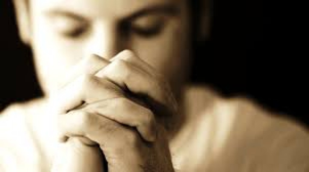 Мужчина сосредоточенно молится скрестив пальцы рук между собой