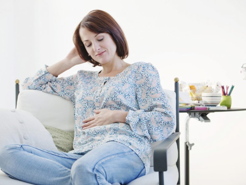 Egy terhes lány ül a kanapén és álmok