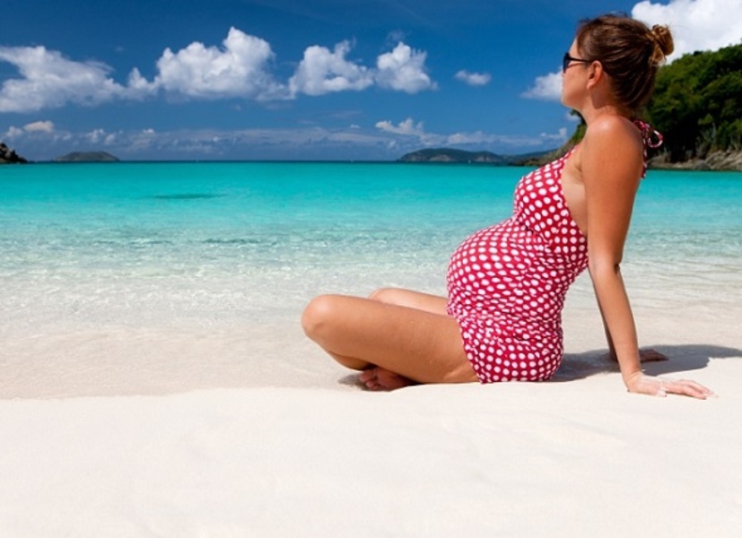 Terhes lány ül a tengerparton a tenger mellett