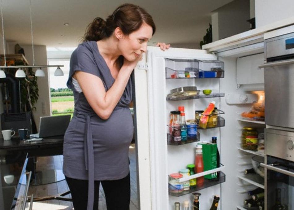 Беременная женщина заглядывает в холодильник