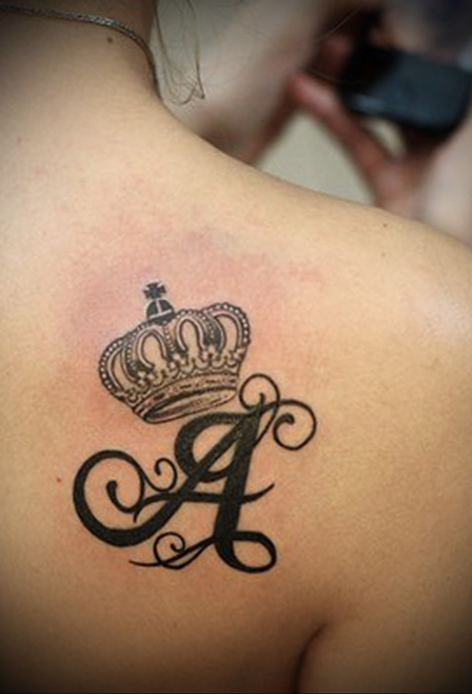 Crown Tatus พร้อมตัวอักษรตัวแรกของชื่อบนใบพัดไหล่ของหญิงสาว